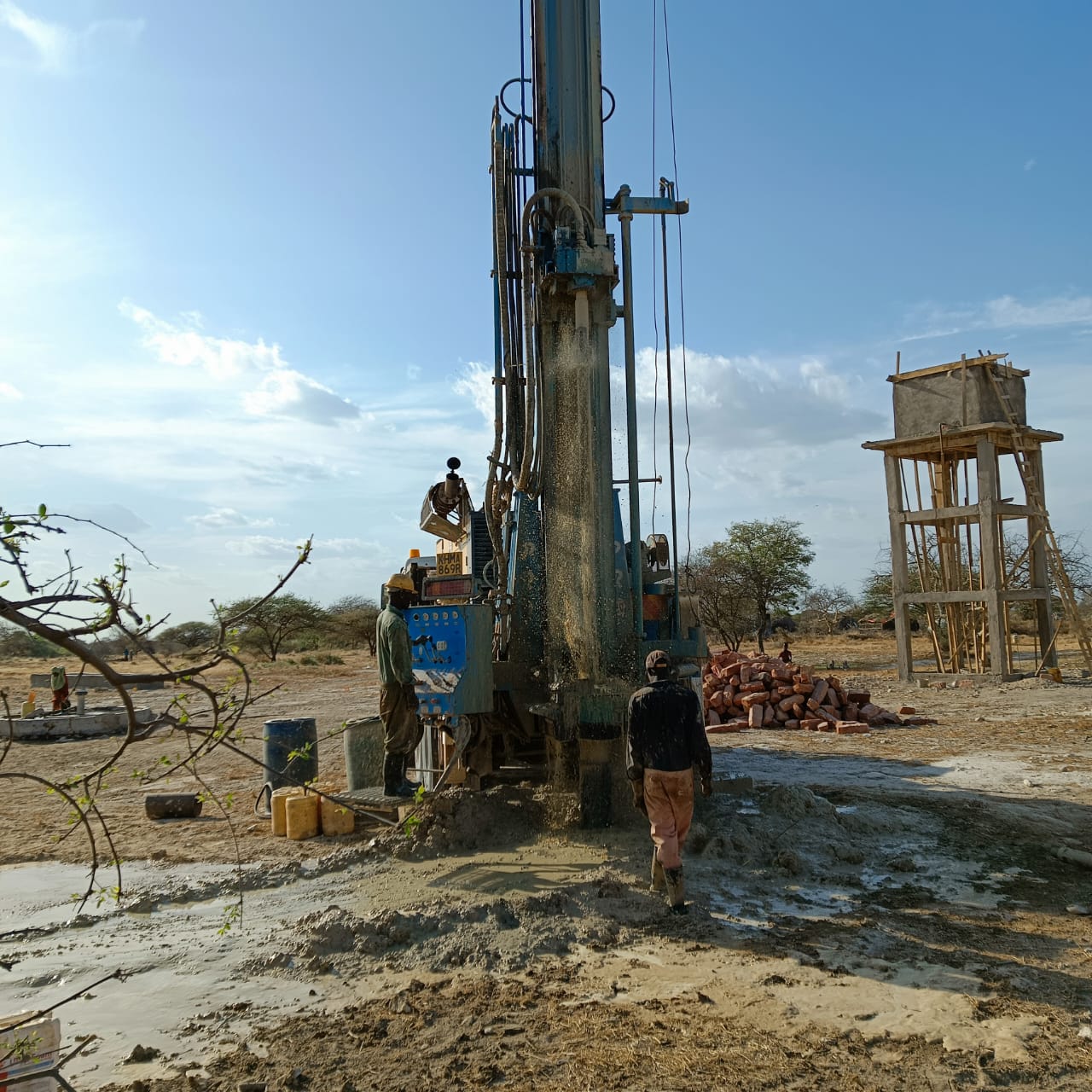 Borehole drilling rig beside water tower under construction